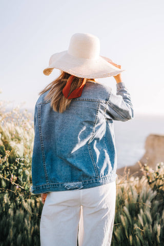 Woman's back wearing a denim jacket and a wide-brimmed hat