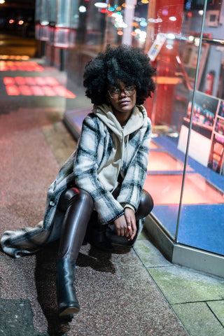 woman sitting on the sidewalk wearing leather pants, a hoodie and a coat