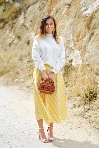 Woman posing with a yellow midi skirt and a white sweater