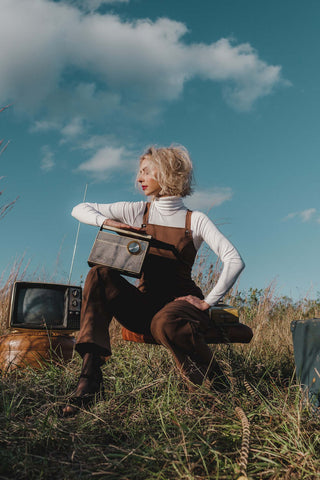Photo of woman posing by old radio stations and TVs and wearing turtleneck sweater under a romper