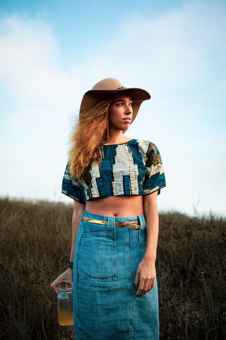 Woman posing in an open field wearing a denim skirt and a patterned top