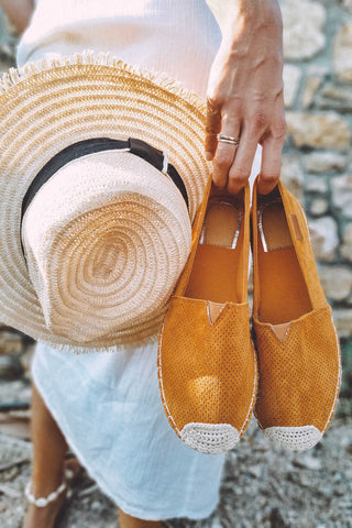 Woman hand holding espadrilles and a wide-brimmed summer hat
