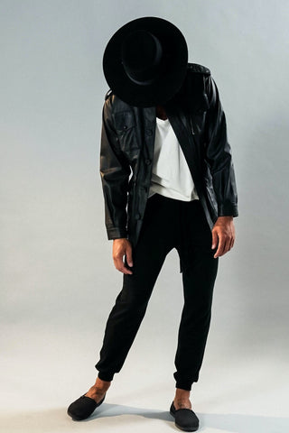 Man in a hat posing in black joggers and leather jacket