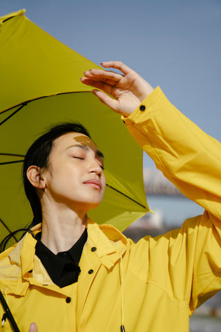 Woman enjoying the sun and wearing a yellow raincoat and umbrella