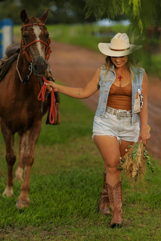 Woman leading a horse wearing shorts with cowboy boots