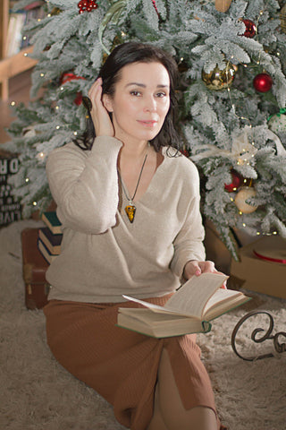 Woman posing next to a Christmas tree in a brown sweater and a midi skirt