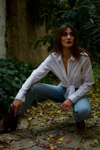 woman posing with a white button up shirt tied in the front and jeans