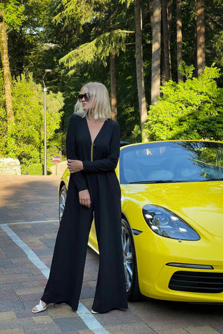 Woman posing in black jumpsuit next to a yellow sports car