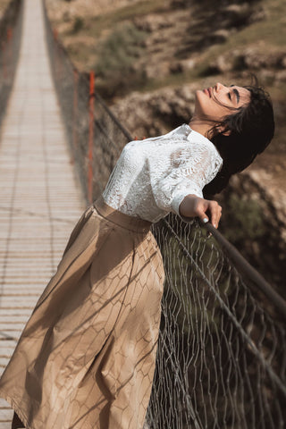 Woman lining on a bridge and posing in a lace shirt and brown midi skirt