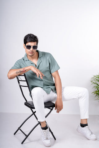 Man posing seated in a short-sleeved shirt and white jeans