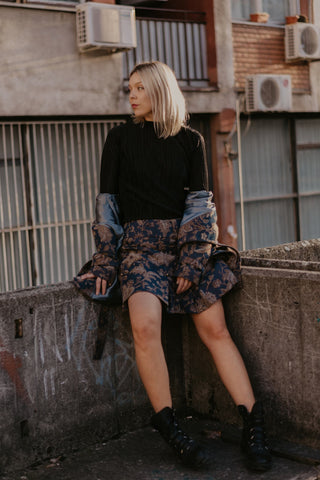 Girl posing on a balcony and wearing a black turtleneck with a floral skirt and ankle boots