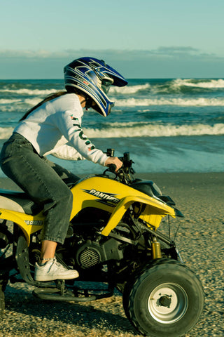 Woman doing quad biking on the beach wearing jeans and sweater