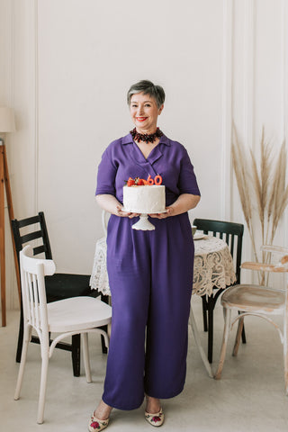 Mature woman holding a cake and wearing a purple jumpsuit