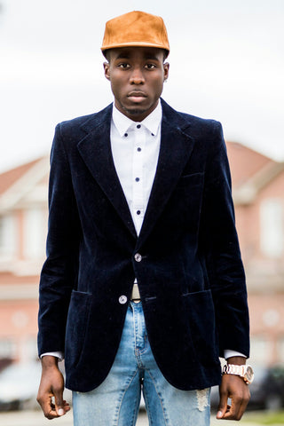 Black young man posing with a navy blue blazer and a baseball cap