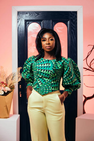Black woman posing with a patterned green blouse and yellow dressy pants