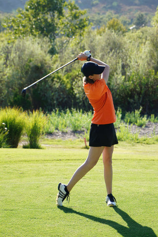 Woman playing golf wearing a skort and an orange polo shirt