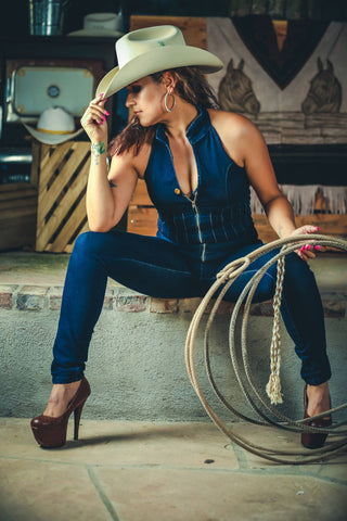 Sexy woman posing for a photo in blu denim well-fitted jumpsuit and a cowboy hat