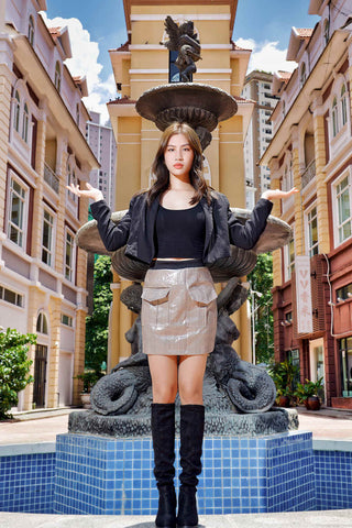 Girl posing in the city and wearing over-the-knee boots, leather skirt and a black cropped blazer