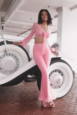 Woman posing for a photo next to a retro car wearing pink flared pants and a bralette top