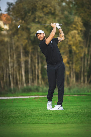 A man playing golf in black chinos and a polo shirt