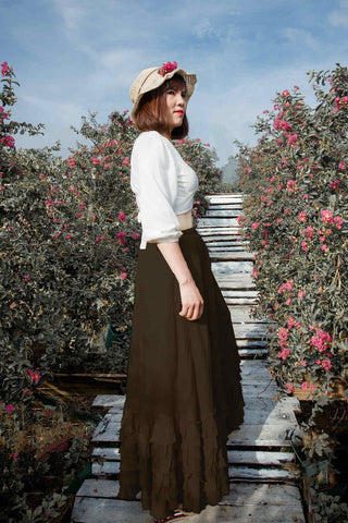 Femme posant dans une longue jupe marron, une chemise blanche et un chapeau à bords