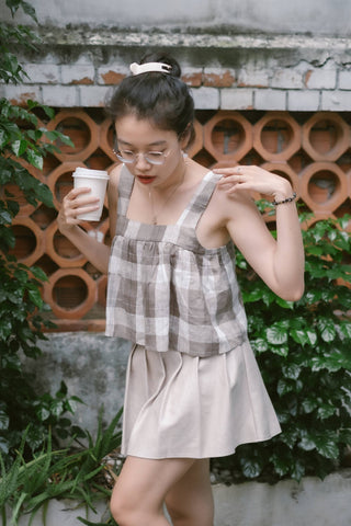 Girl holding a cup and wearing a beige mini skirt and a sleeveless top