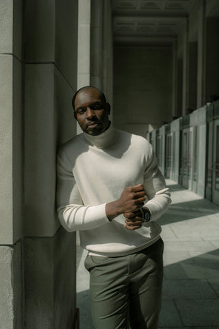 Black man posing with a white turtleneck and khaki pants