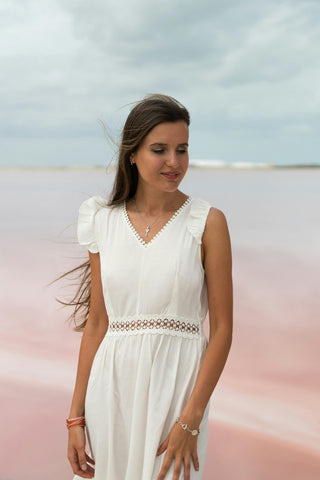 Frau posiert am Meer mit einem weißen Sommerkleid