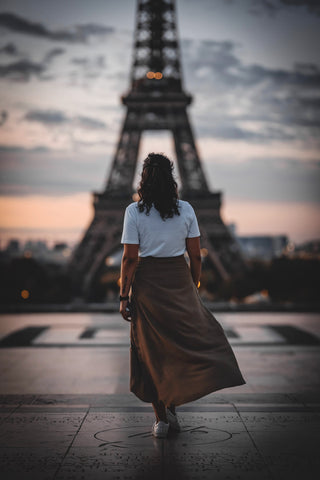 Photo of the back of a woman wearing long brown skirt, white t-shirt and sneakers