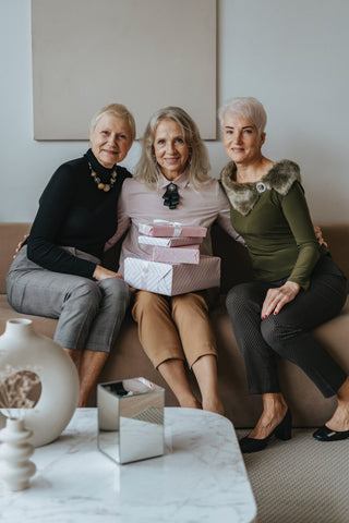 Three mature women posing with gifts and wearing chino pants and nice tops