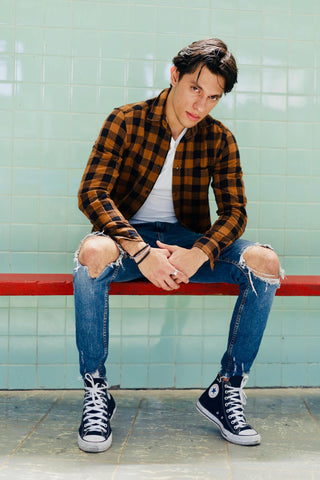 Young man posing sitting with ripped jeans and a flannel shirt over a tee