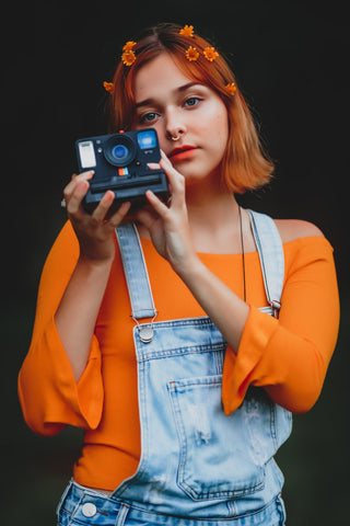 Young woman holding a camera and wearing an off-the-shoulder top with rompers