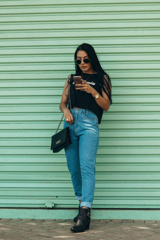 Girl holding a phone wearing high waist jeans, a top, and ankle boots