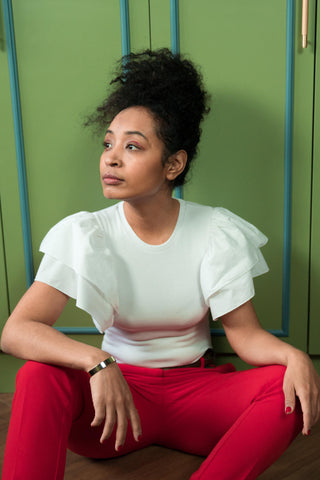 woman posing sitting with a white ruffled blouse and red chinos