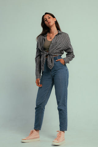 Frau posiert in einer hoch taillierten Jeans, einem Tanktop und einem Hemd zum Binden vorne