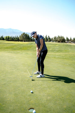 Woman on a golf course practicing putting and wearing leggings and a top
