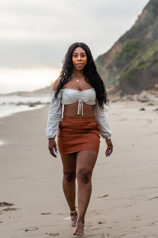 Woman walking on the beach in brown mini skirt and a white crop top