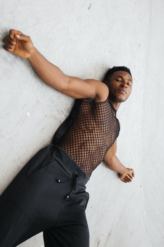 Man laying on a wall and wearing sweatpants with a fishnet top