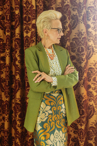 Elderly woman posing in a green blazer and a patterned top and skirt