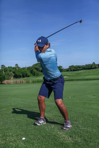 A man performing a golf swing in blue shorts and polo shirt