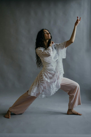 Frau in Yoga-Pose mit weißer Tunika und fließender Hose