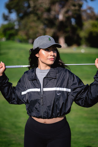 Woman holding a golf stick wearing a cropped lightweight jacket