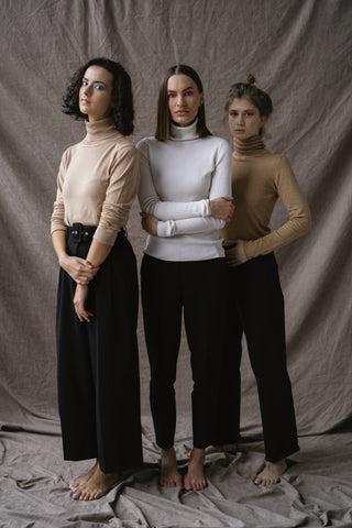 Three women posing for a photo wearing turtle-neck sweaters and black pants