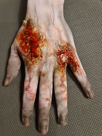 hånd med zombiesår lavet med blod, latex og sminke på grå baggrund