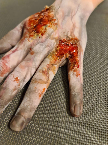 hånd med zombiesår lavet af latex, blod og sminke med grå baggrund