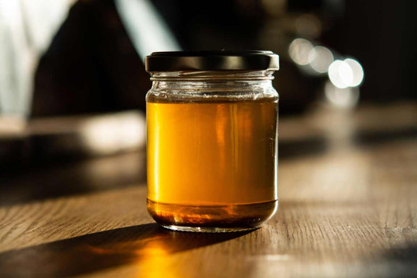 Rainbow Bees Organic Hawaiian Honey jar sitting on a table. Lehua Honey ready to be used in a dish.