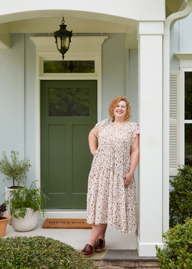 Homeowner Ashley Whiteside stands on the porch of her home painted in Clare’s gray exterior paint color, Grayish. The front door is painted with Daily Greens.
