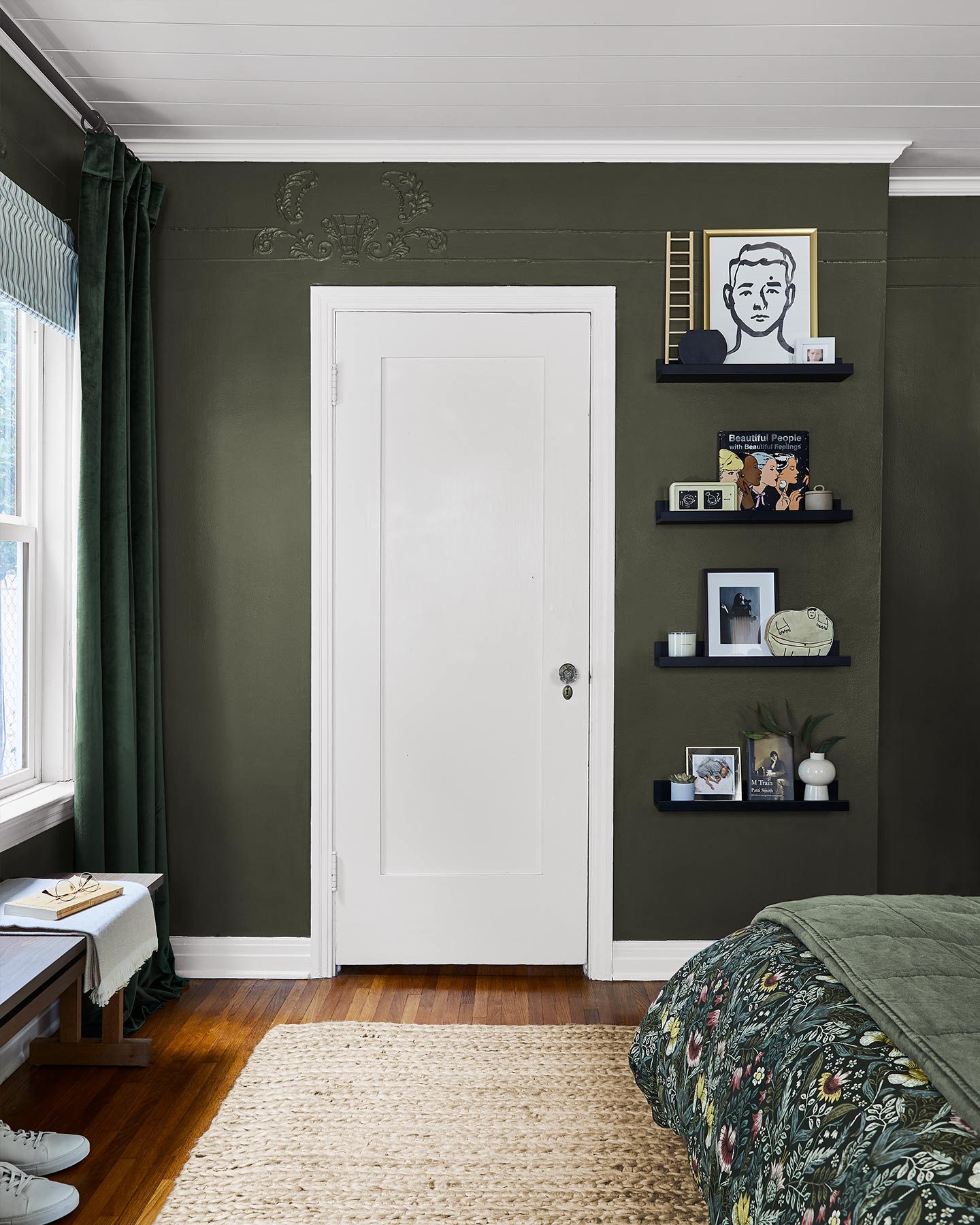 Dark drapes and black salon-style shelving are perfect complements in this dark green bedroom.