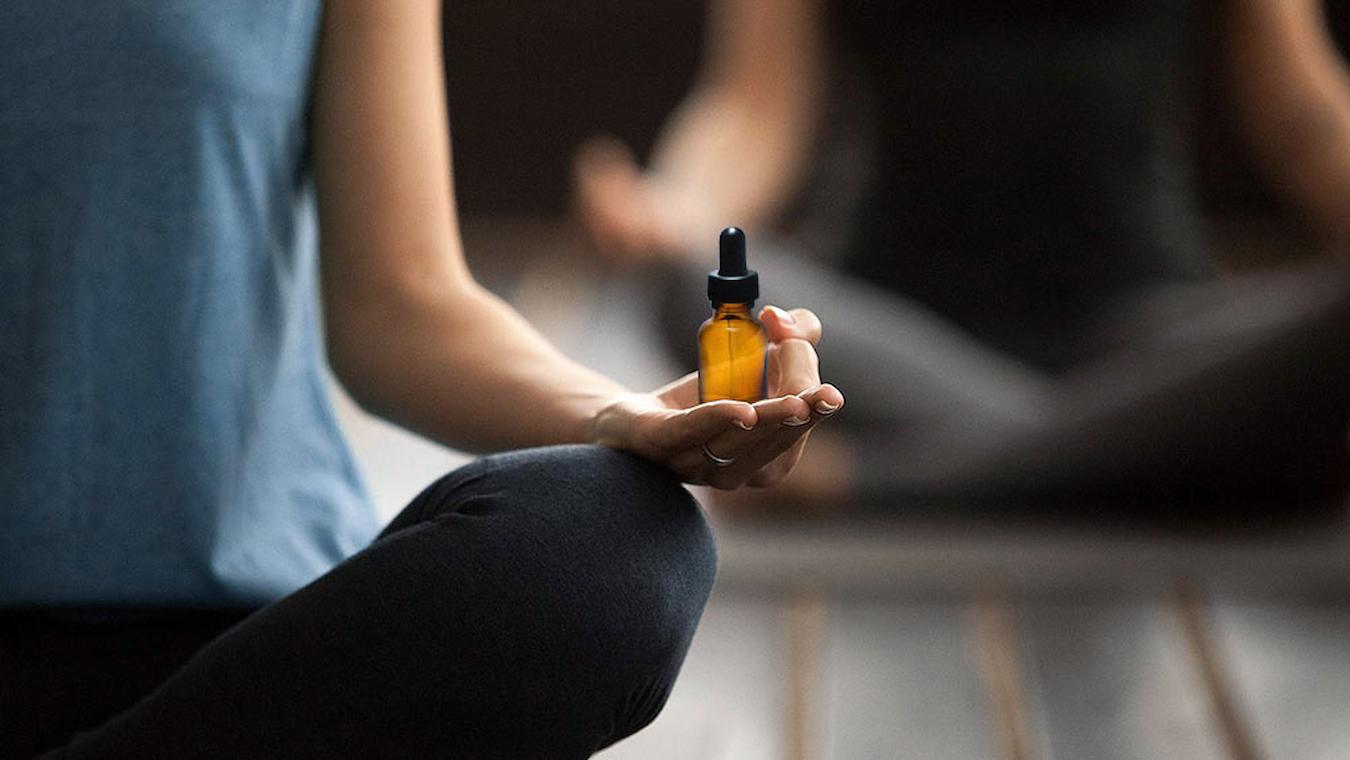 someone holding a dropper bottle while meditating physical discomfort daily cbd oils broad spectrum daily lives calm calm meditate stress focus mood