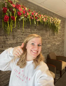 Andi Gretzinger in front of a wood flower hanging arch installation